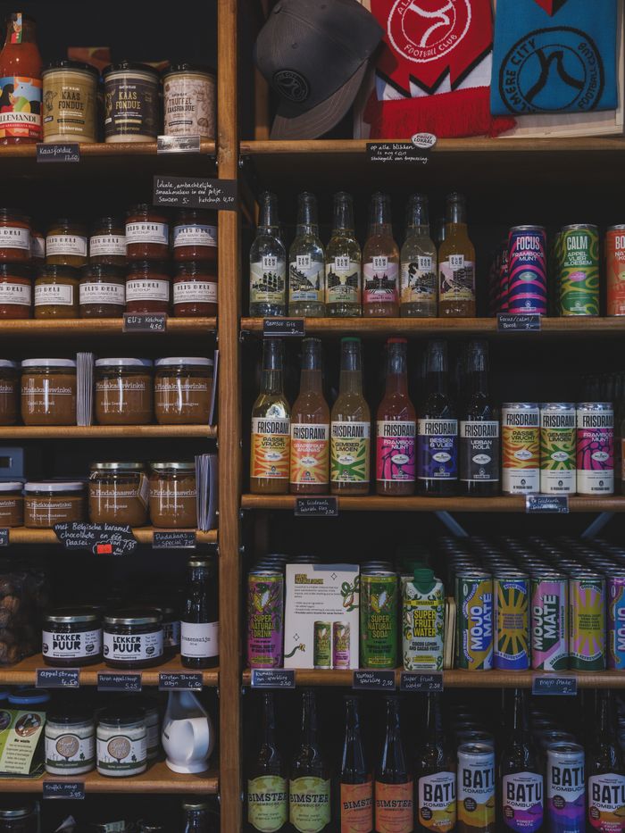A variety of artisanal food items like jam, honey, and drinks displayed on wooden shelves in a local store.